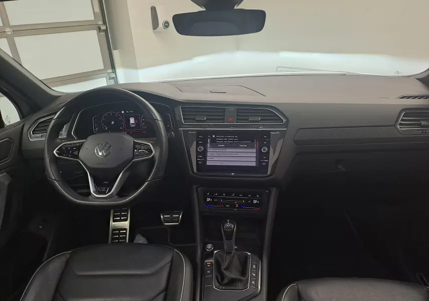 Vue intérieure frontale du Volkswagen Tiguan 2024, tableau de bord noir avec écran tactile et volant multifonction.