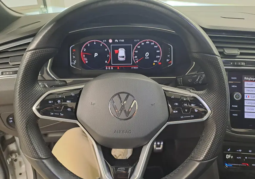 Vue intérieure centrée sur le volant perforé du Volkswagen Tiguan 2024 avec tableau de bord digital et commandes intégrées.
