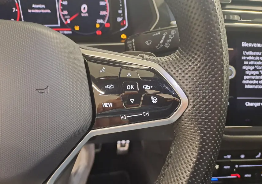 Gros plan sur le volant perforé côté droit du Volkswagen Tiguan 2024, avec commandes intégrées et affichage numérique en arrière-plan.