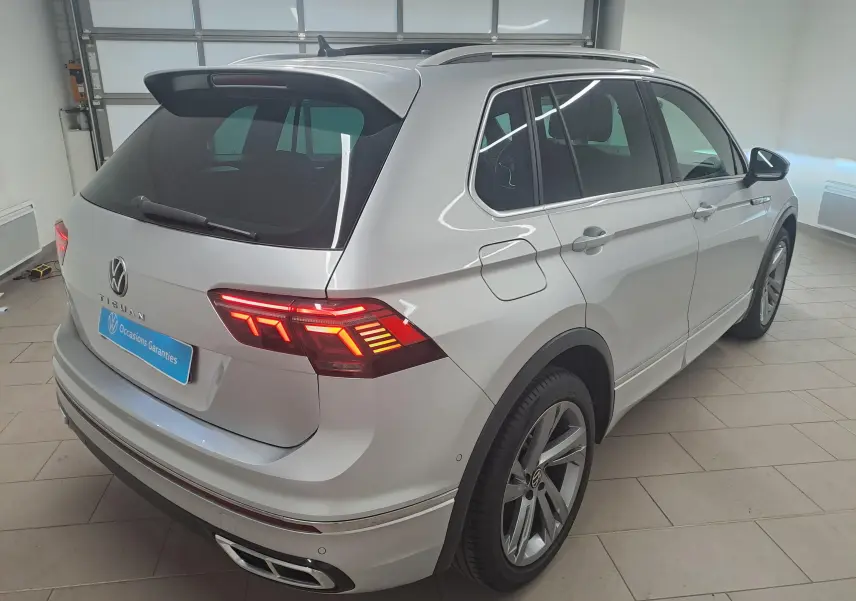 Vue 3/4 arrière droite du Volkswagen Tiguan 2024 en Reflet d'Argent avec feux LED et attelage escamotable visible.