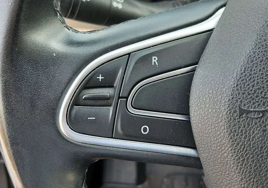 Gros plan sur les commandes gauche du volant noir du Renault Scénic IV gris Cassiopée, avec boutons de réglage et cruise control.