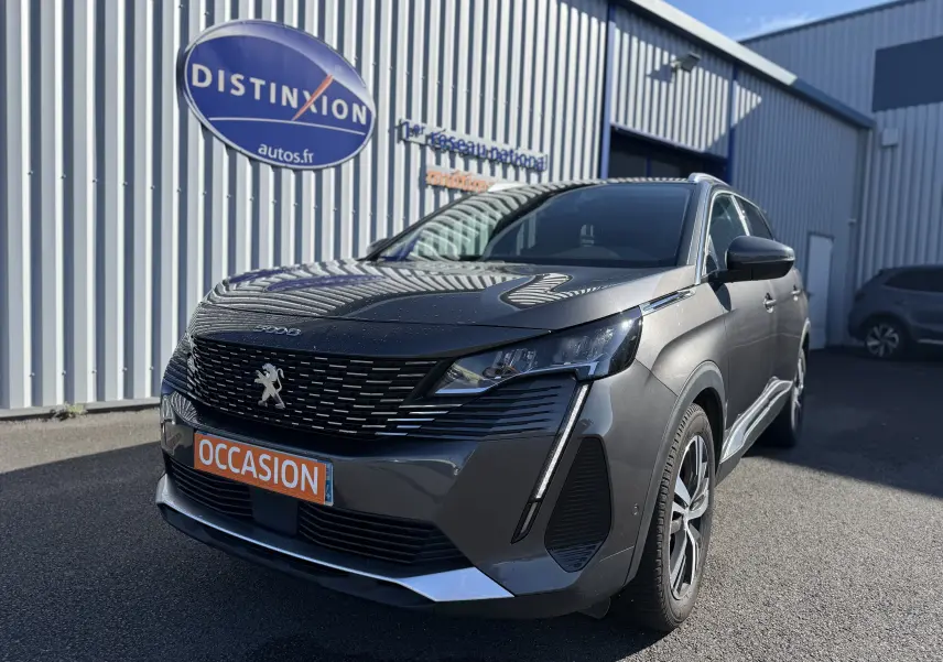 Peugeot 5008 gris en 3/4 avant droit, avec calandre noire et plaque orange "OCCASION" visible devant un bâtiment.