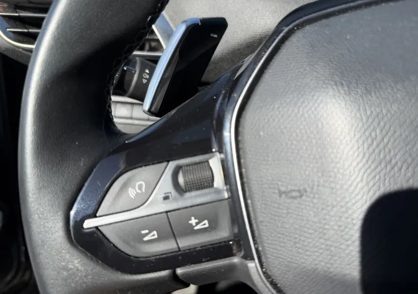 Gros plan sur la partie gauche du volant noir du Peugeot 5008 2021 avec commandes audio et régulateur de volume.