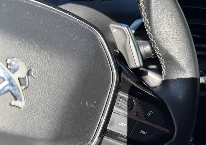 Gros plan sur le volant noir du Peugeot 5008 1.5 HDI 130 Allure, avec commandes audio et palette de changement de vitesse.