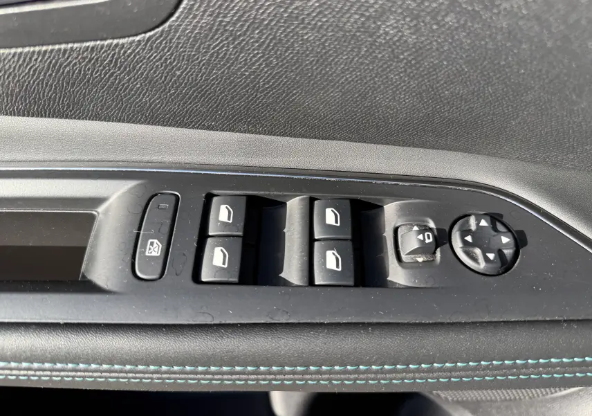 Gros plan sur les commandes de lève-vitres et réglage des rétroviseurs côté conducteur du Peugeot 5008 gris, intérieur noir.