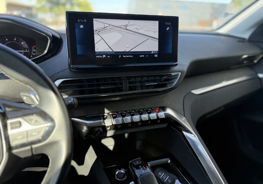 Vue intérieure centrée sur la console centrale et l'écran tactile du Peugeot 5008 gris, avec commandes et levier de boîte automatique visibles.