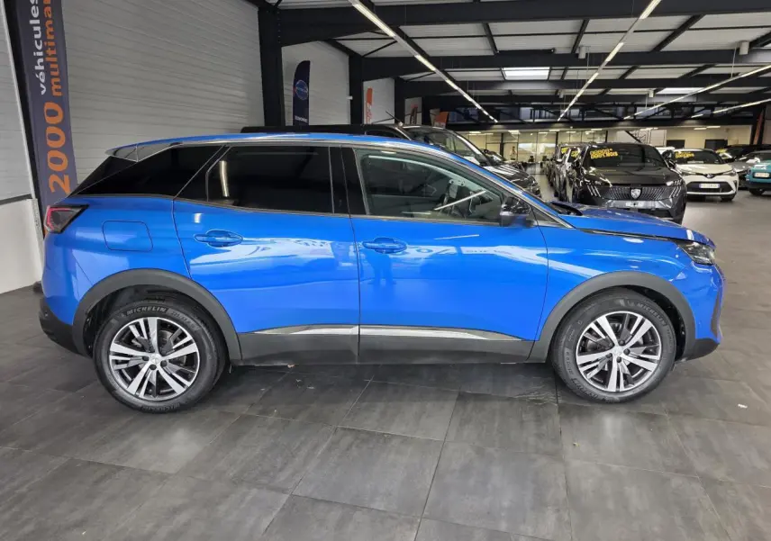 Vue de profil côté gauche d'un Peugeot 3008 2022 bleu Iron avec jantes alliage bicolores en showroom.