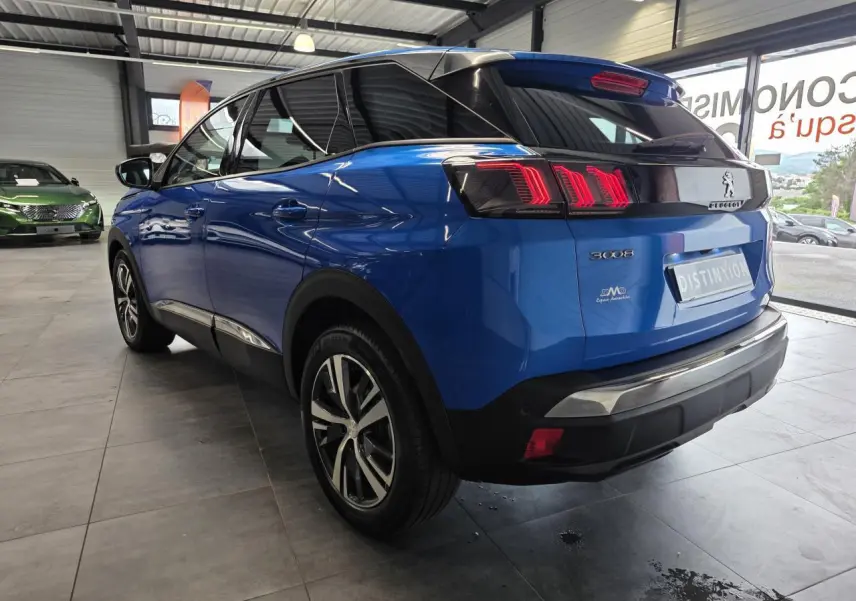 Peugeot 3008 bleu Iron vue 3/4 arrière droit en showroom, avec jantes alliage bi-ton et feux LED distinctifs.