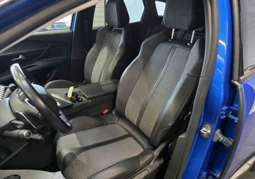 Vue intérieure côté conducteur du Peugeot 3008 Bleu Iron 2022, sièges en tissu et cuir TEP bicolore avec accoudoir central ouvert.