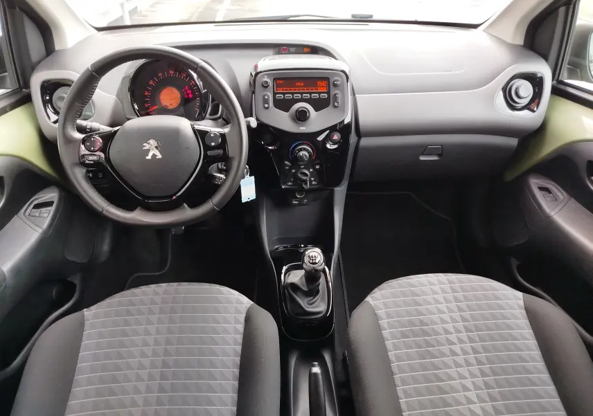 Vue intérieure avant de la Peugeot 108 2021, volant multifonction, tableau de bord noir et sièges gris à motifs géométriques.