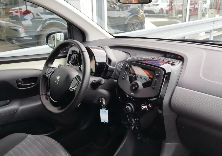 Intérieur de la Peugeot 108 2021 vu côté conducteur, tableau de bord noir avec volant multifonction et console centrale brillante.