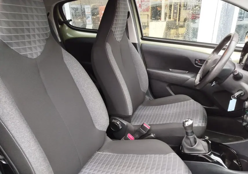 Vue intérieure côté conducteur de la Peugeot 108 2021, sièges tissu gris à motifs géométriques et volant multifonction.
