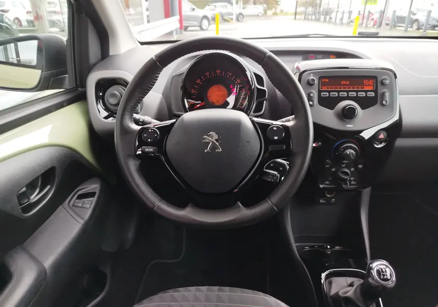 Vue intérieure centrée sur le volant Peugeot, tableau de bord avec affichage orange et levier de vitesses manuel.