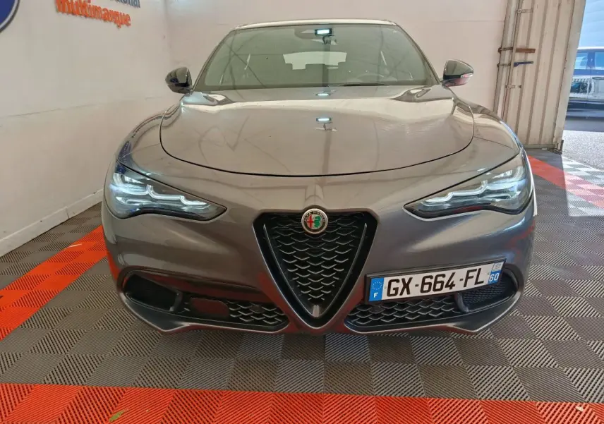 Vue frontale d'un Alfa Romeo Stelvio gris foncé 2024 avec calandre caractéristique en V et phares LED allumés.
