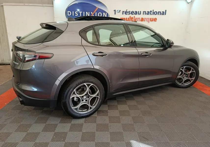Vue côté gauche d'un Alfa Romeo Stelvio gris foncé 2024 avec jantes sport et feux arrière LED dans un showroom.