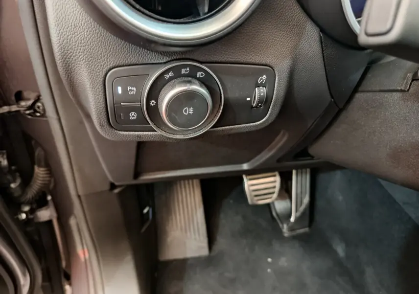 Gros plan sur les commandes d'éclairage et les pédales côté conducteur de l'Alfa Romeo Stelvio gris foncé 2024.