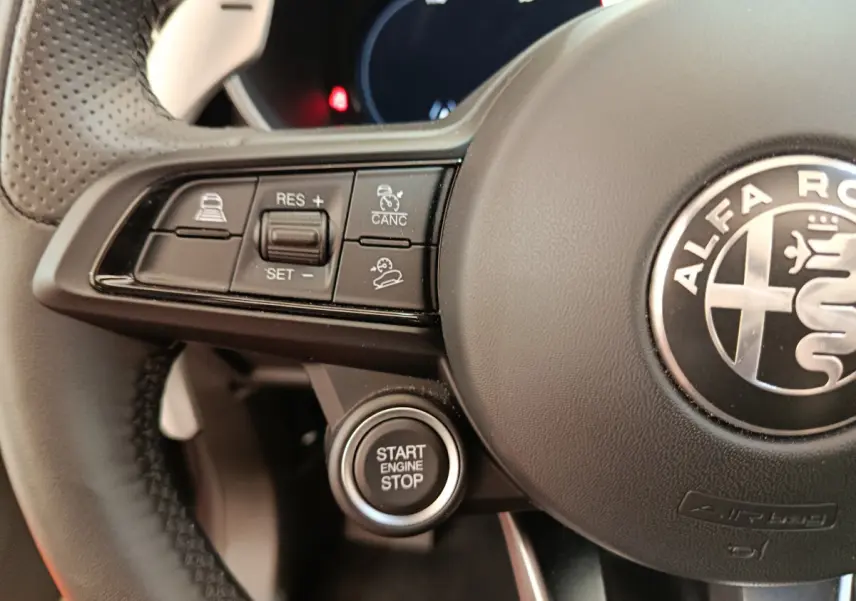 Gros plan sur le volant cuir perforé de l'Alfa Romeo Stelvio gris foncé avec commandes de régulateur et bouton start/stop.