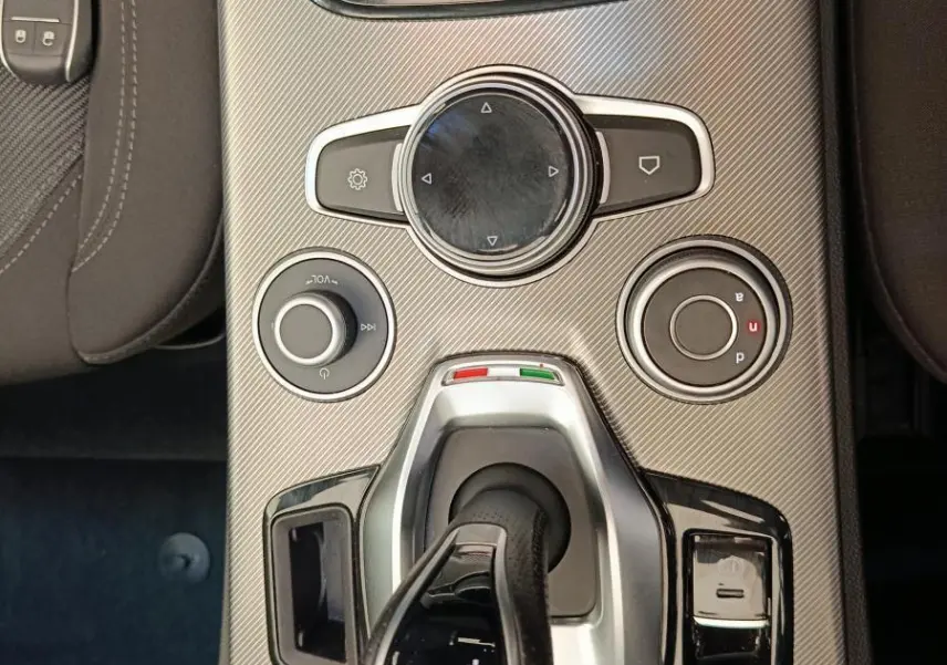 Vue plongeante sur la console centrale gris foncé de l'Alfa Romeo Stelvio avec levier de vitesses automatique et commandes rotatives.