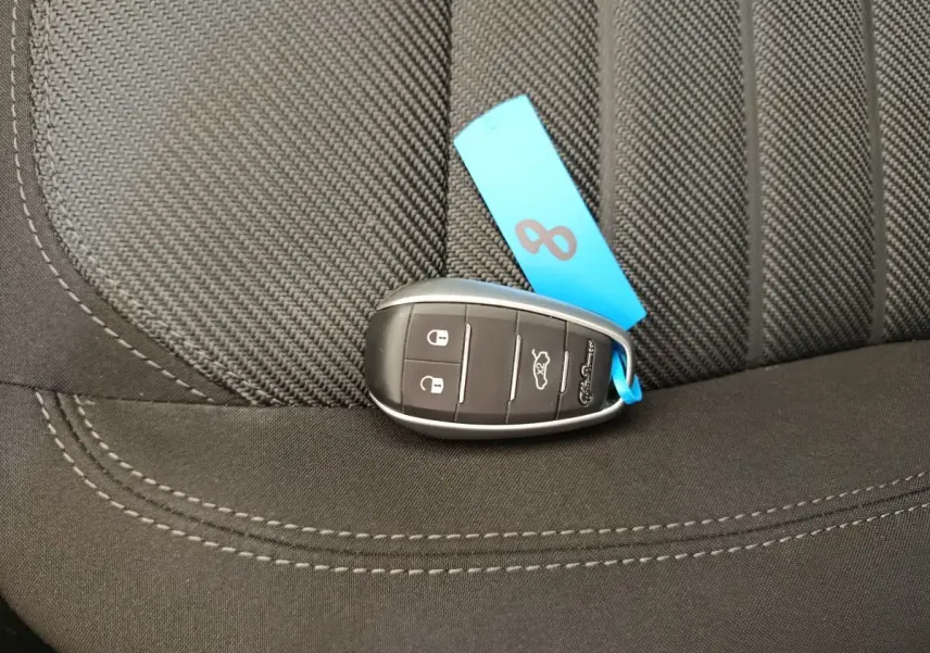 Gros plan sur clé de voiture Alfa Romeo Stelvio posée sur siège tissu gris foncé avec étiquette bleue.