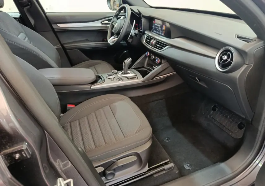 Intérieur côté passager de l'Alfa Romeo Stelvio gris foncé 2024, avec tableau de bord moderne et sièges tissu noirs.