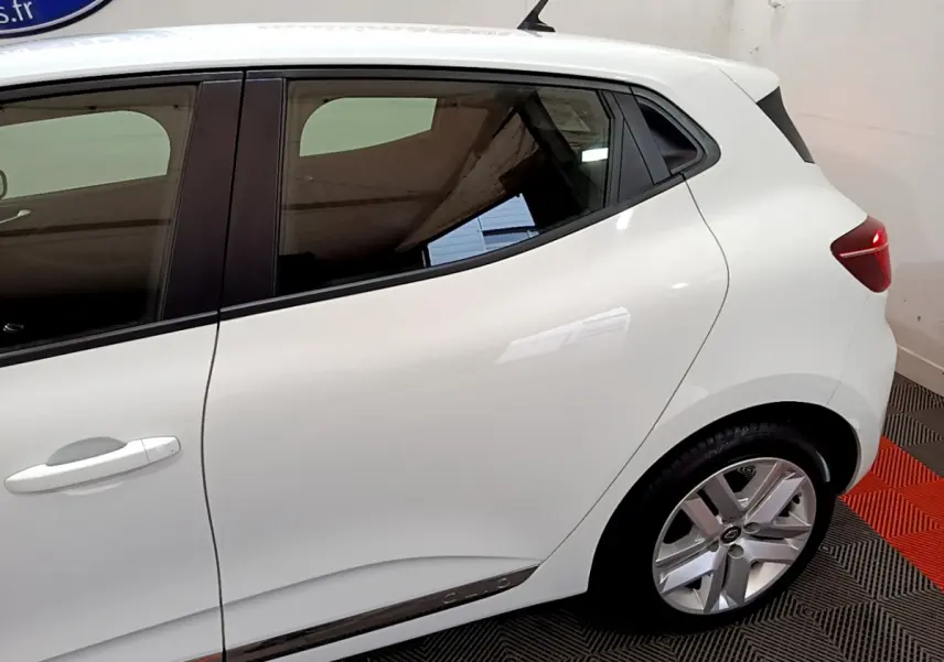 Vue côté gauche arrière d'une Renault Clio Business TCe 90 blanche avec jante alliage et feux arrière allumés.