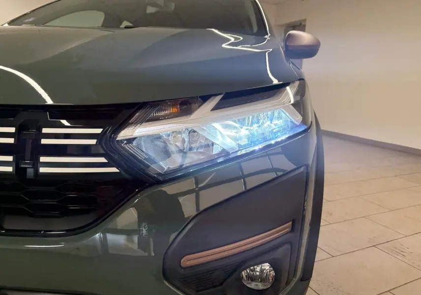 Gros plan sur l'avant droit vert cèdre du Dacia Sandero Stepway 2023 avec phare allumé et calandre noire.
