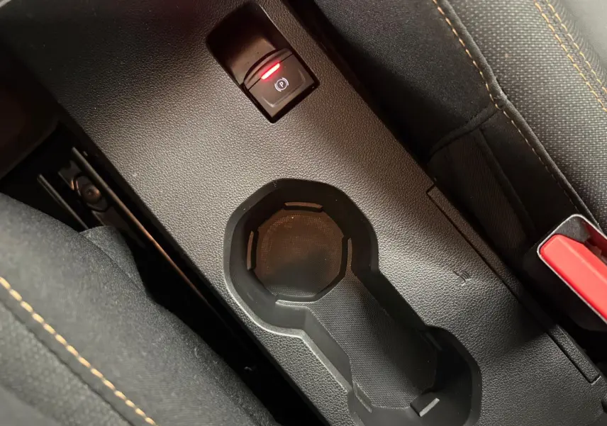 Gros plan sur la console centrale noire du Dacia Sandero Stepway 2023 avec porte-gobelets et frein à main électrique.