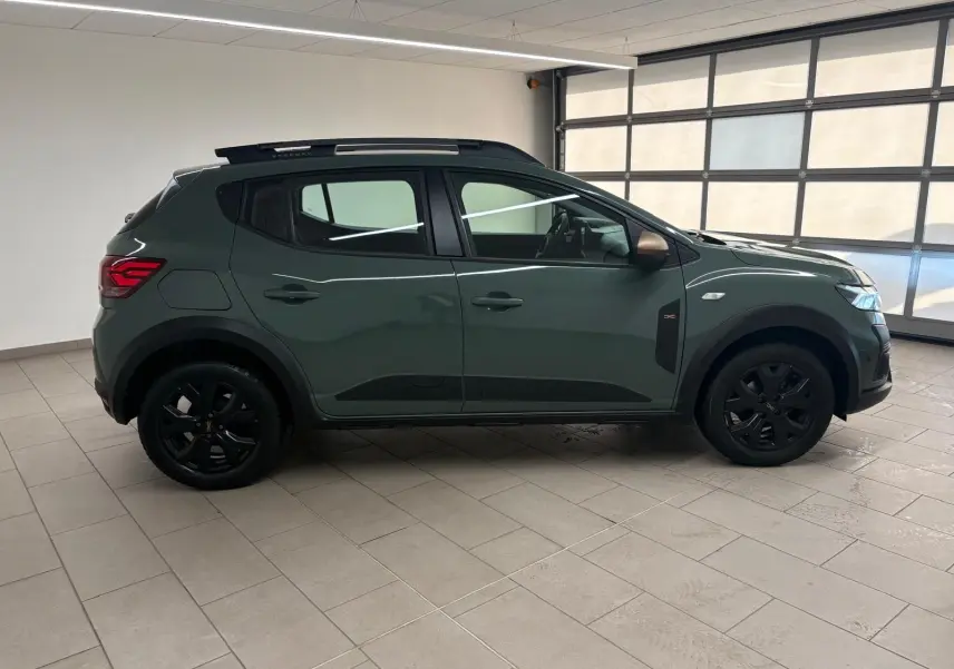 Vue latérale droite d'une Dacia Sandero Stepway 2023 vert cèdre avec jantes noires et attelage visible.