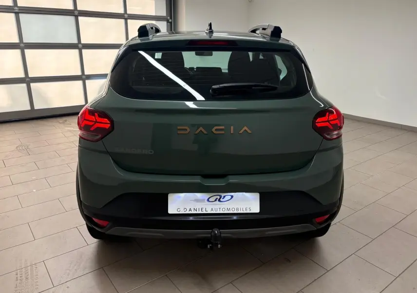 Vue arrière d'une Dacia Sandero Stepway 2023 vert cèdre avec feux allumés et attelage visible en intérieur.
