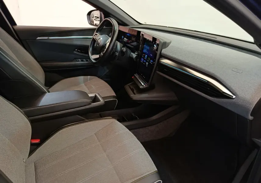Intérieur avant droit de la Renault Mégane Techno EV60 220ch, sièges gris, grand écran tactile vertical et volant cuir.