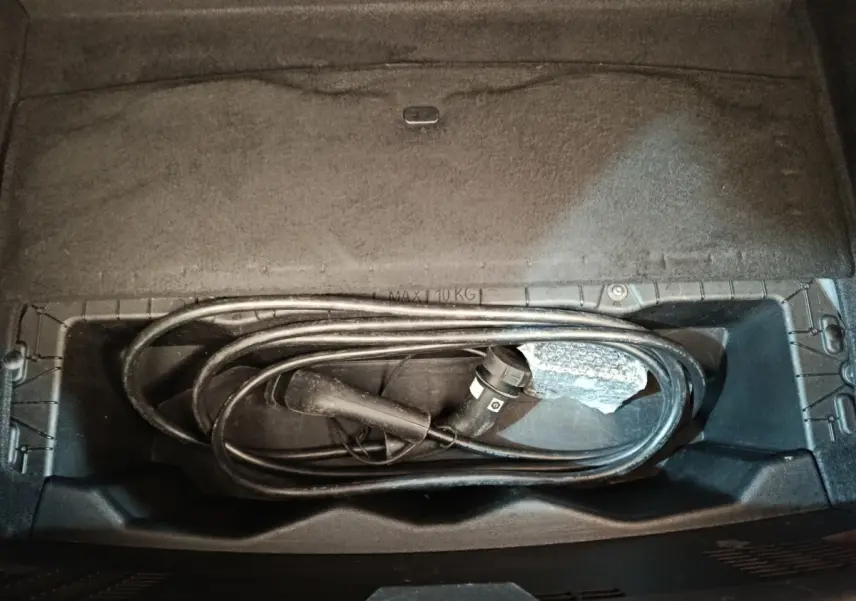 Vue plongeante sur le rangement sous siège arrière d'une Renault Mégane électrique avec câble de recharge noir enroulé.
