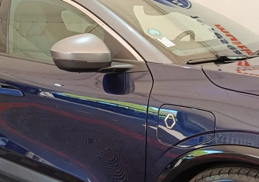 Vue latérale gauche rapprochée de la Renault Megane Techno EV60 bleu avec rétroviseur argenté et prise de recharge électrique.