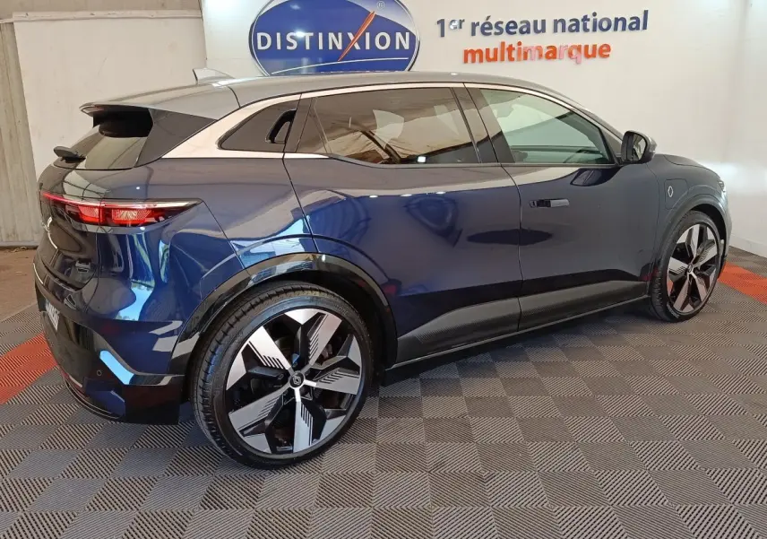 Renault Mégane Techno EV60 bleu en 3/4 arrière droit, jantes modernes et toit contrasté argenté visible en intérieur showroom.