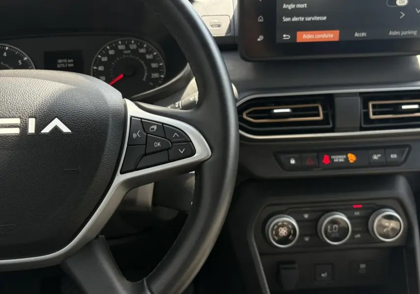 Gros plan sur le volant Dacia et la console centrale avec écran tactile et commandes de climatisation du Sandero Stepway.