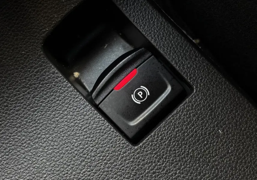 Gros plan sur le bouton de frein de parking électrique avec témoin rouge dans l'habitacle noir du Dacia Sandero Stepway.