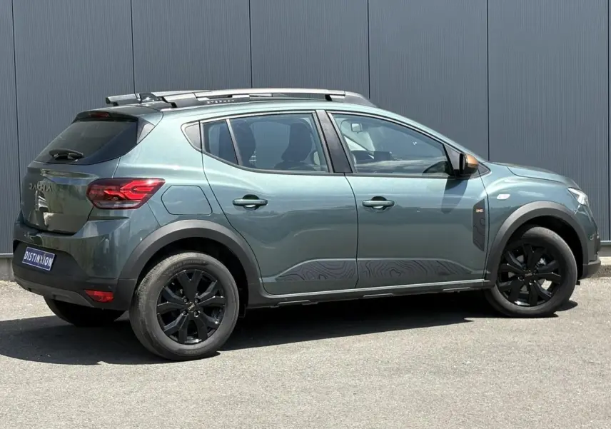 Vue de profil côté droit d'une Dacia Sandero Stepway Vert Cèdre avec jantes noires et barres de toit gris Mégalithe.