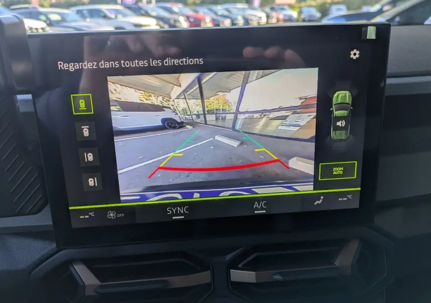 Écran tactile montrant la caméra de recul d’un Dacia Bigster bleu indigo avec lignes de guidage colorées.