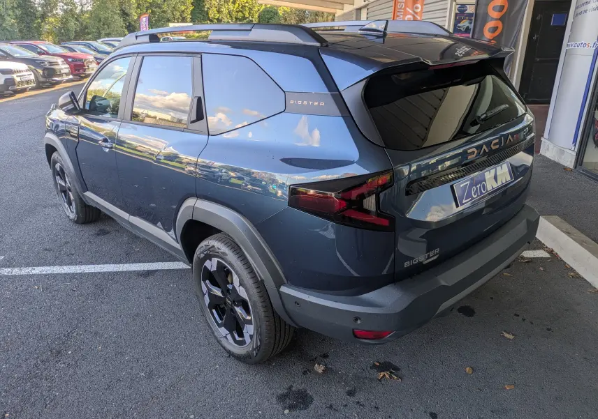 Vue 3/4 arrière droite du Dacia Bigster Hybrid 155 Extreme bleu indigo avec jantes noires et barres de toit.