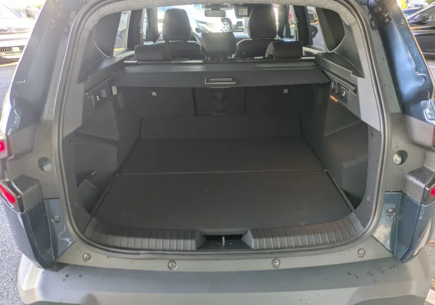 Coffre ouvert vu de l'arrière du Dacia Bigster Hybrid 155 Extreme bleu indigo, montrant l'espace de chargement avec cache-bagages.
