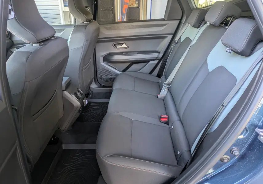 Vue latérale droite de l'intérieur arrière du Dacia Bigster Hybrid 155 Extreme bleu indigo, sièges tissu noirs et ceintures visibles.