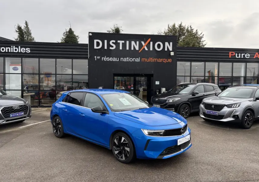Opel Astra VI bleu clair vue 3/4 avant droit avec jantes noires devant concession Distinxion