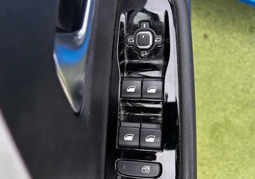 Gros plan sur les commandes de lève-vitres et rétroviseurs sur la porte côté gauche d'une Opel Astra bleu clair.