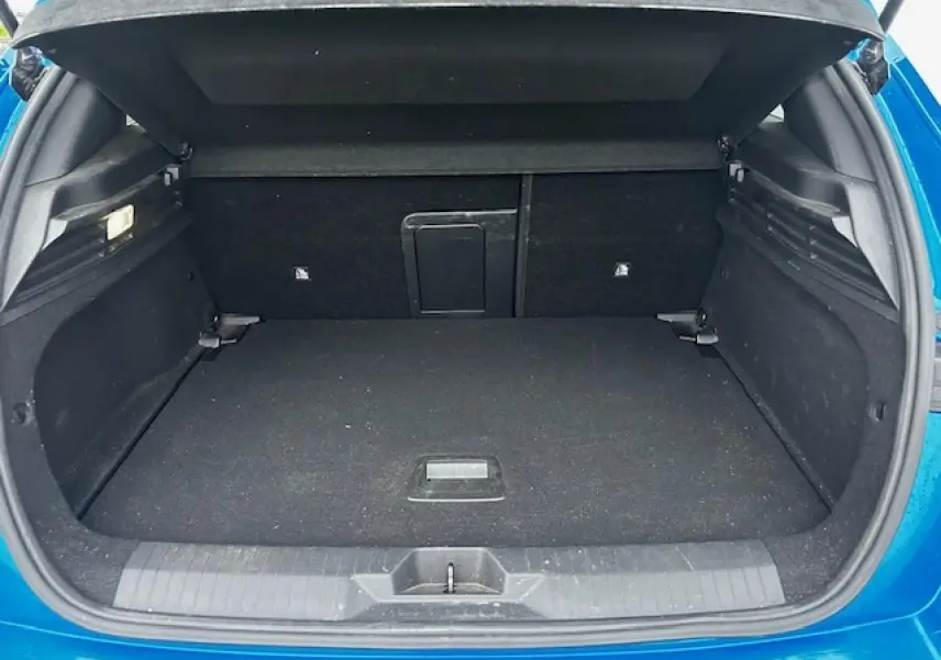 Coffre ouvert de l'Opel Astra bleu clair, vue arrière montrant l'espace de chargement et la trappe à skis intégrée.