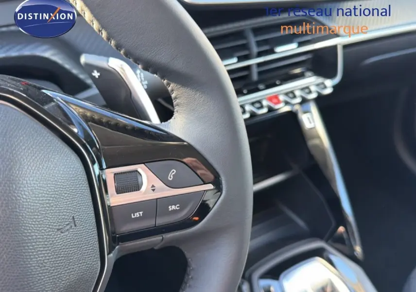 Gros plan sur le volant cuir noir et les commandes multimédia de la Peugeot 208 hybride 2025, intérieur moderne