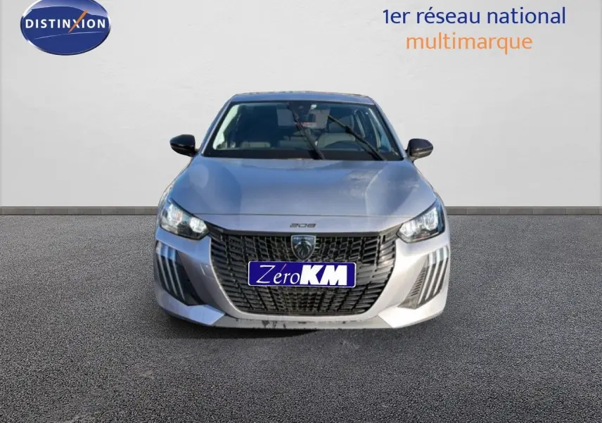 Vue frontale d'une Peugeot 208 gris artense métal 2025 avec calandre noire et phares LED allumés.