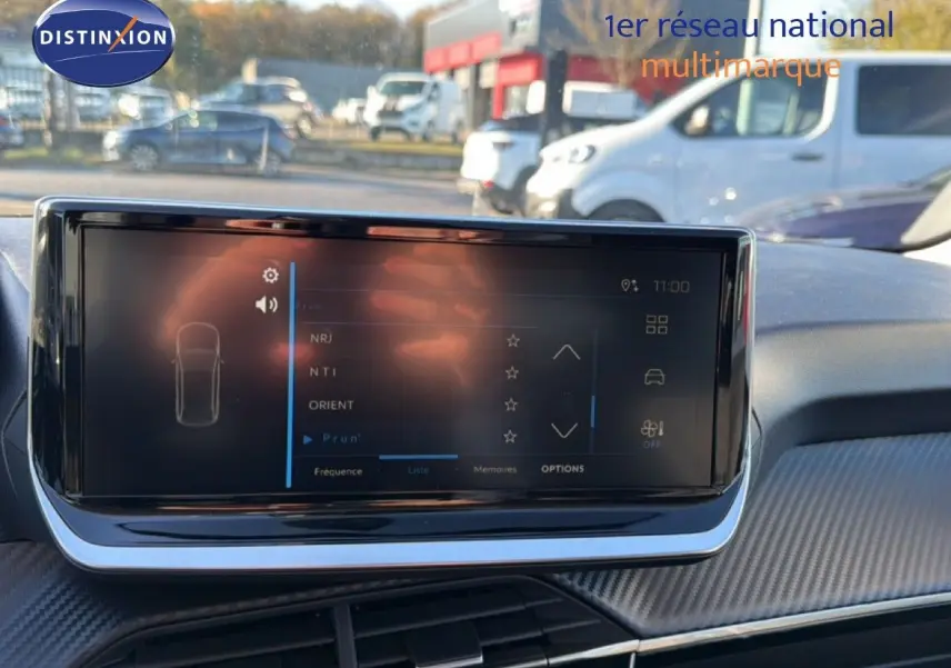Écran tactile central du tableau de bord de la Peugeot 208 hybride 2025 avec finition gris artense métal visible à l'extérieur.