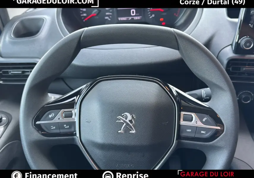 Vue rapprochée du volant Peugeot Rifter bleu 2024, avec commandes intégrées et tableau de bord numérique en arrière-plan.