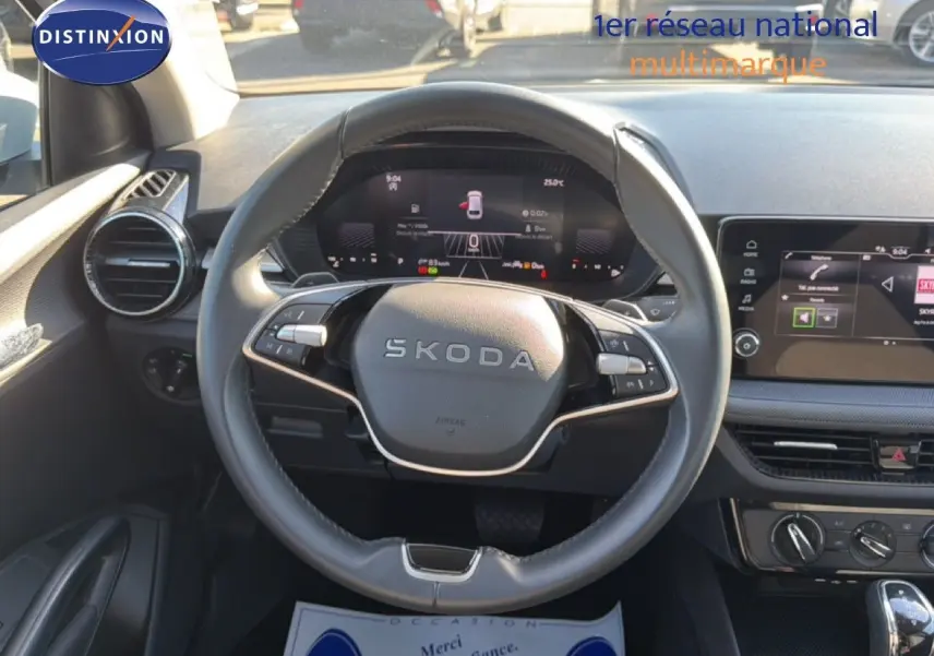 Vue intérieure centrée sur le volant SKODA d'une Fabia blanche, avec tableau de bord digital et écran tactile visible.