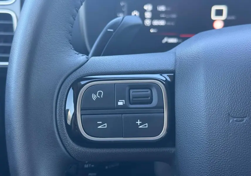 Gros plan sur les commandes gauche du volant cuir noir du Citroën C5 Aircross 2025, avec boutons multifonctions.
