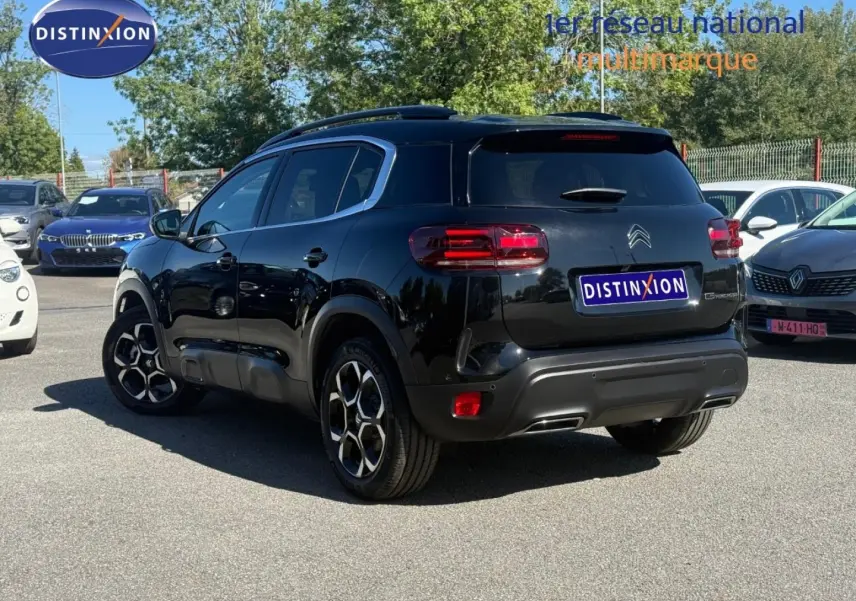 Vue 3/4 arrière droite d'un Citroën C5 Aircross noir Perla Nera avec jantes alu et barres de toit visibles.